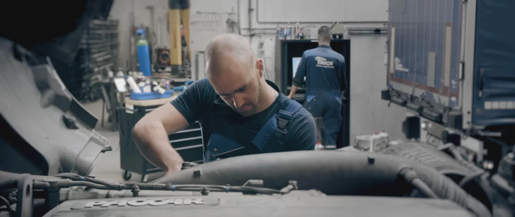 Een man die aan een motor werkt in de werkplaats van Becx Verhuur, omringd door gereedschap en onderdelen van voertuigen.