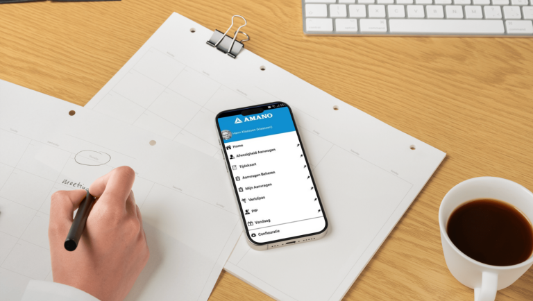 Een werknemer schrijft in een notitieblok terwijl een smartphone op het bureau ligt.