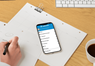 Een werknemer schrijft in een notitieblok terwijl een smartphone op het bureau ligt.